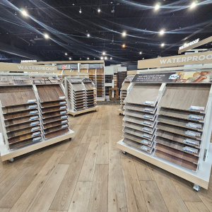 Kalamazoo, MI flooring showroom with mobile display racks showcasing waterproof and hardwood flooring samples in various wood tones, under bright industrial lighting.